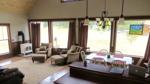 A spacious living area with a kitchen, dining table, and large windows offering a view of the outdoors.