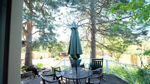Een terras met een ronde tafel en stoelen, een groene parasol en een witte reling.
