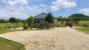 A rustic house with a gravel driveway, surrounded by greenery and a clear sky.