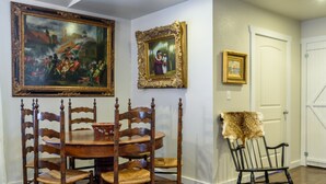 A dining room with a wooden table and chairs, framed artwork on the walls, and a door with a white frame.