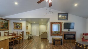 A spacious living area with a wooden floor, a dining table with chairs, a sofa, a television, and a fireplace.