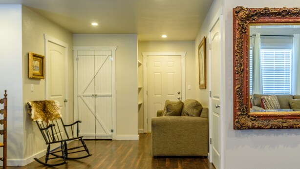 A hallway with wooden flooring, a rocking chair, a couch, and a large ornate mirror.