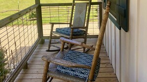 A wooden porch with two rocking chairs, a view of a grassy field, and a building in the background.