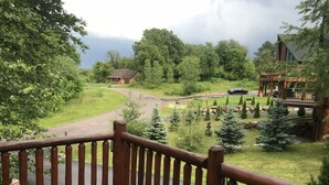 A wooden deck with a view of a lodge and a winding road surrounded by trees. - Hana Log Cabin near Devil's Lake (Baraboo)