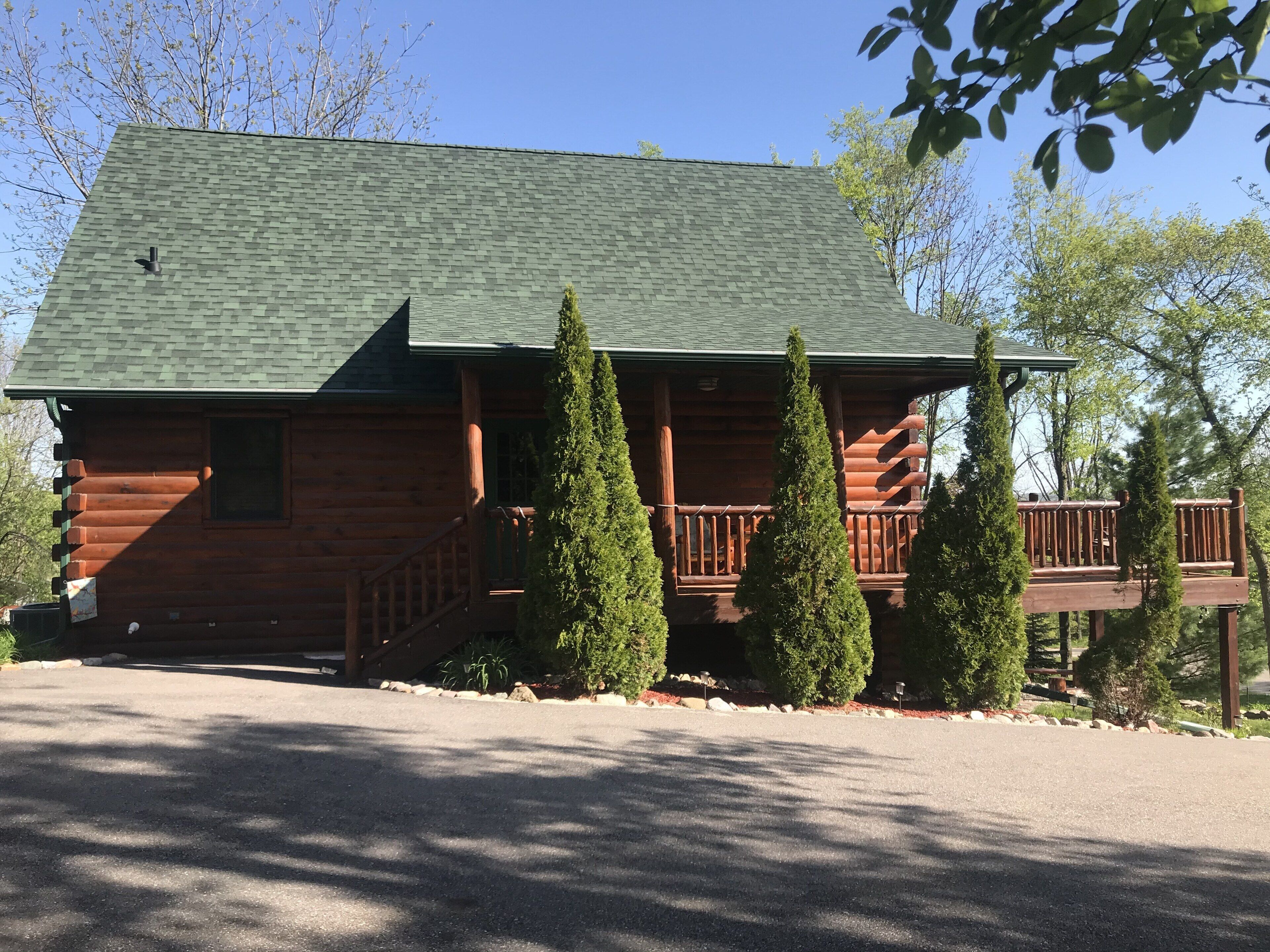 A log cabin with a green roof, a front porch, and a deck.