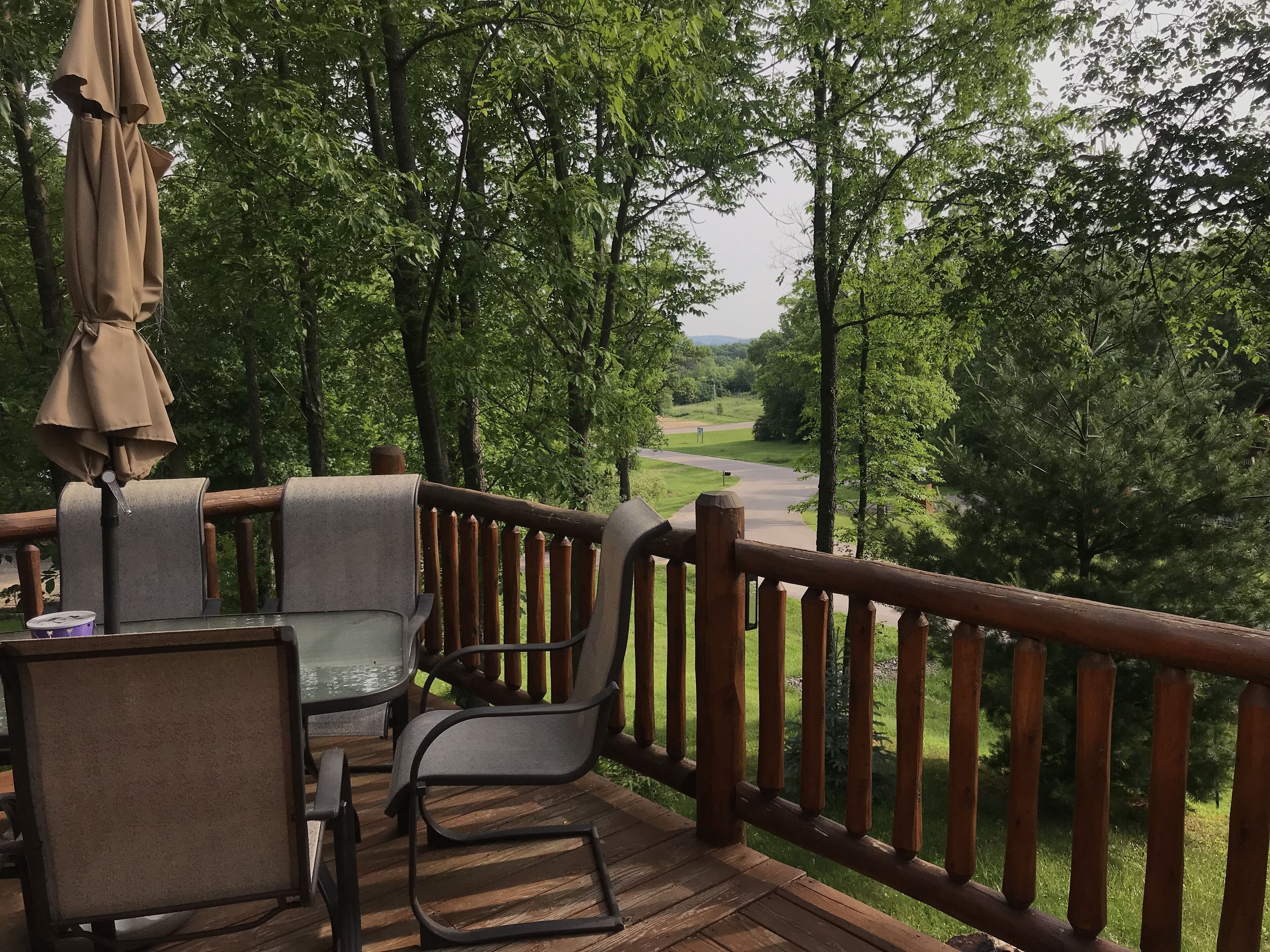 Terraza de madera con mesa y sillas, con vista a un área boscosa.