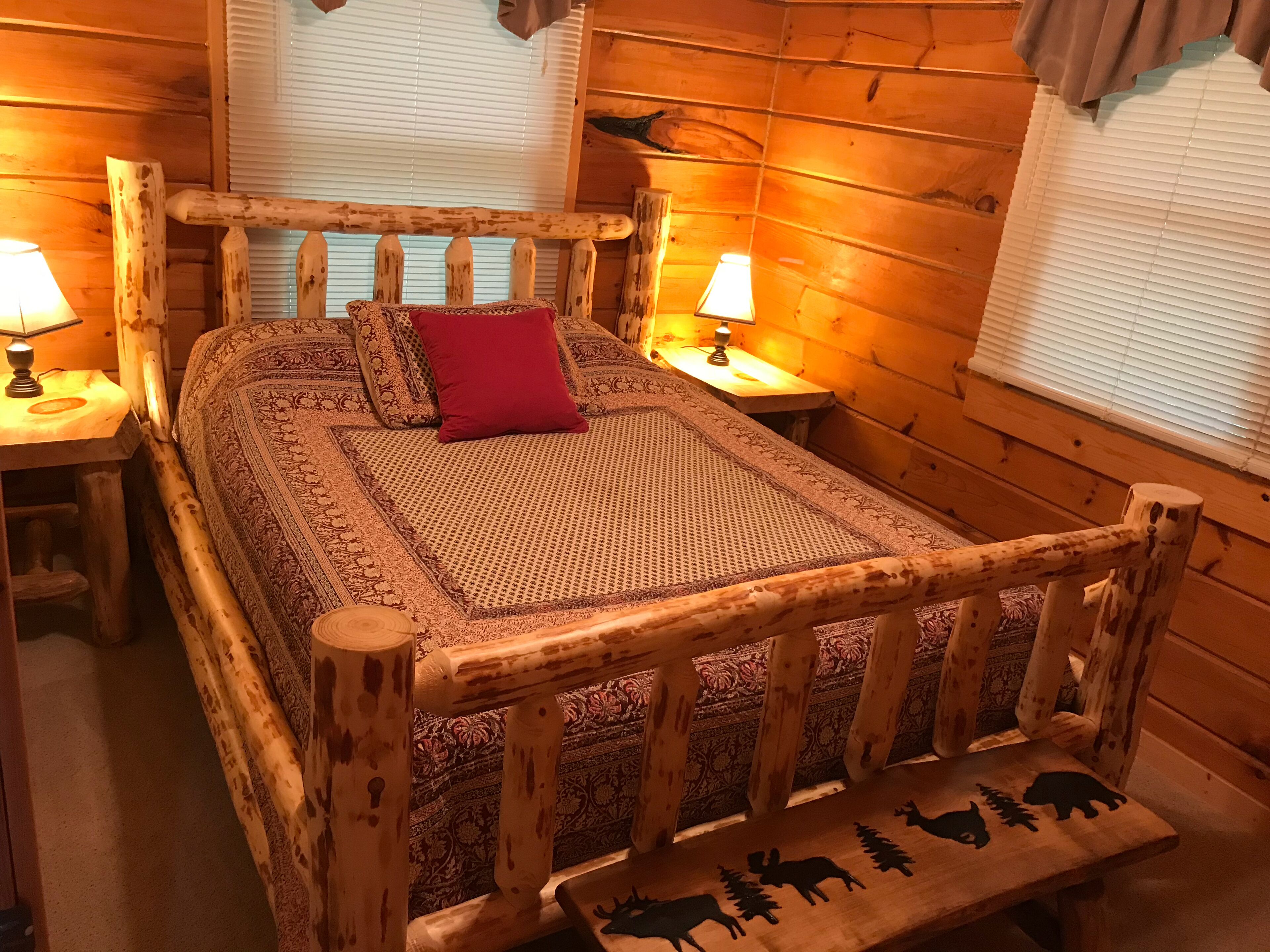 Ein Bett mit Holzkopfstütze, zwei Nachttische, ein rotes Kopfkissen und geblümtes Bettzeug.
