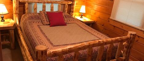 Ein Bett mit Holzkopfstütze, zwei Nachttische, ein rotes Kopfkissen und geblümtes Bettzeug.