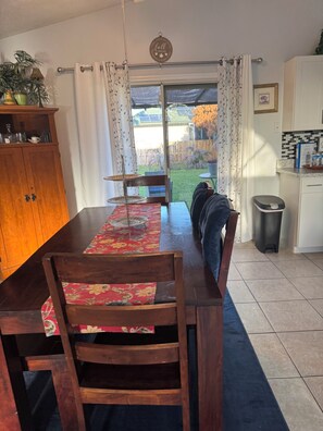 Un comedor con una mesa de madera, sillas, un tapete estampado y vistas al patio trasero a través de una puerta de vidrio.