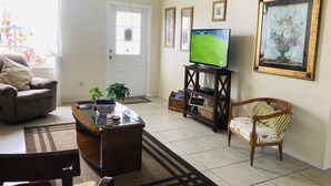 A living room with a sofa, a wooden coffee table, a television on a stand, a chair, and a door.