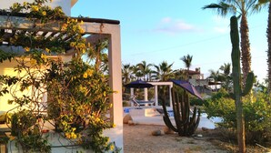 Eine Terrasse mit Tisch und Stühlen, eine Pergola mit Kletterpflanzen und ein Poolbereich mit Sonnenschirmen.