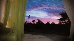 Ein Zimmer mit Blick auf einen Sonnenuntergangshimmel durch ein Fenster mit Vorhängen.
