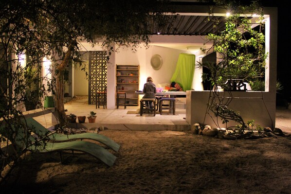 An outdoor patio area with a dining table and chairs, surrounded by potted plants and a bookshelf. - Cozy lounge with pool and atmosphere (Todos Santos)