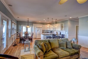 A spacious living room with a green sofa, wooden flooring, and a kitchen in the background.