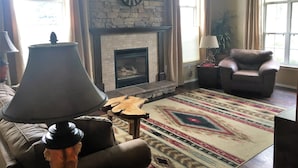 A living room with a fireplace, a clock, a ceiling fan, and a leather armchair. - Peak View Retreat, 3 Bedroom Sleeps 6 (Flagstaff)