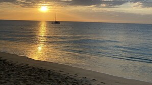 Una playa con un velero en aguas tranquilas durante el atardecer.