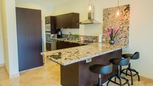 Una cocina moderna con encimeras de granito, armarios oscuros, campana extractora de acero inoxidable y una zona de bar con taburetes.