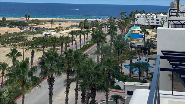 Vista de playa con palmeras, una piscina y un edificio de techo azul.