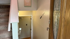 Ein Flur mit einer zur Toilette führenden Tür, einem Willkommen-Schild und einer Holztür mit Fenster.
