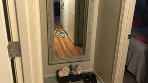 Ein Flur mit einem Spiegel, der einen Raum, eine Tür und einen Schuhregal mit Hausschuhen widerspiegelt.