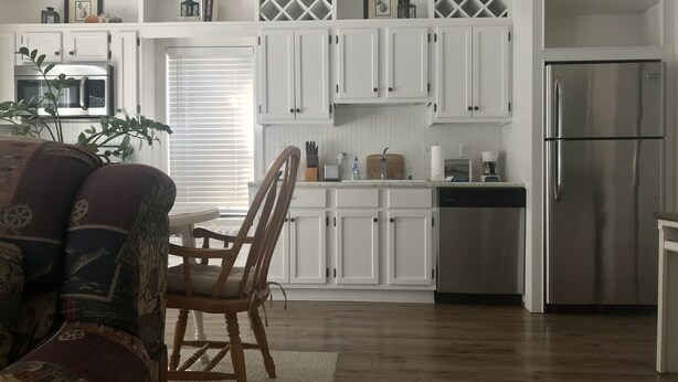 Una cocina moderna con armarios blancos, electrodomésticos de acero inoxidable y un comedor con mesa y sillas de madera.