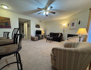 A living room with a ceiling fan, a TV, a fireplace, and a dining area with chairs and a table.