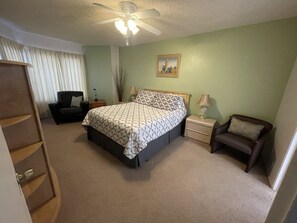 A bedroom with a bed, two bedside tables, a chair, a ceiling fan, and a painting on the wall.