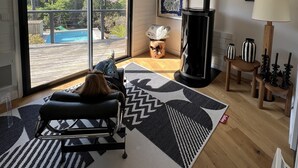 Ein geräumiges Wohnzimmer mit einem großen Schiebeglastür, die auf eine Terrasse führt, einem Kamin und Blick auf einen Swimmingpool.