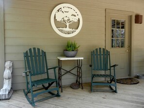 Une véranda avec deux fauteuils à bascule, une petite table sur laquelle est posée une plante en pot, et une porte avec une fenêtre.