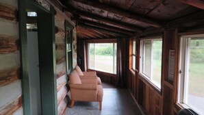 A cabin interior with a wooden ceiling, a bench along the wall, and a window with a view of the outdoors. - Rustic Lakeside Log Cabins (Renfrew)