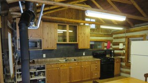 A rustic kitchen with wooden cabinets, a stove, a sink, and a refrigerator. - Rustic Lakeside Log Cabins (Renfrew)