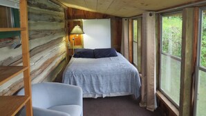 A cabin room with a bed, a chair, a lamp, and a window with curtains. - Rustic Lakeside Log Cabins (Renfrew)