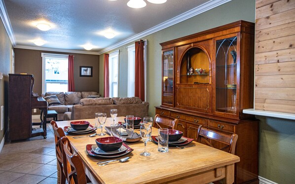 A dining area with a wooden table set for four, surrounded by chairs. A wooden cabinet with glass doors is to the right. - Spacious 3 bedroom home. Minutes from the ski hill. Pets welcome.  (Revelstoke)