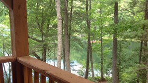 A wooden deck with a view of a forest and a body of water. - Ultimate relaxing vacation  (Orwell)