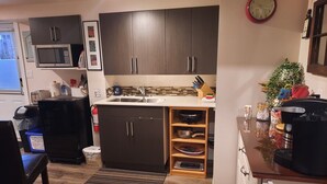 A compact kitchen with dark cabinets, a microwave, a sink, and a small countertop with various items.