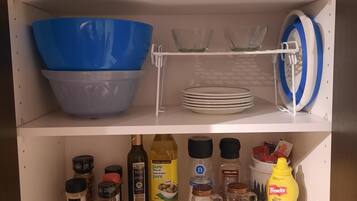 Un meuble de cuisine doté d’étagères contenant divers ustensiles, notamment un saladier bleu, une théière blanche et une tasse à café.