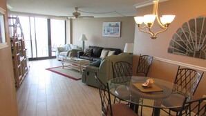 A spacious living area with a dining table, chairs, and a sofa. There is a ceiling fan, a lamp, and a painting on the wall. - Marco Island Remodeled Condo, SSNW, T4, 1408 2 Bd, 2 Ba, SPECTACULAR Sunsets 365 (Marco Island)