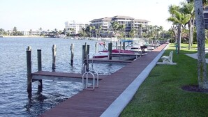 A wooden dock extending into calm water, with a grassy area and palm trees on the right. - Marco Island Remodeled Condo, SSNW, T4, 1408 2 Bd, 2 Ba, SPECTACULAR Sunsets 365 (Marco Island)