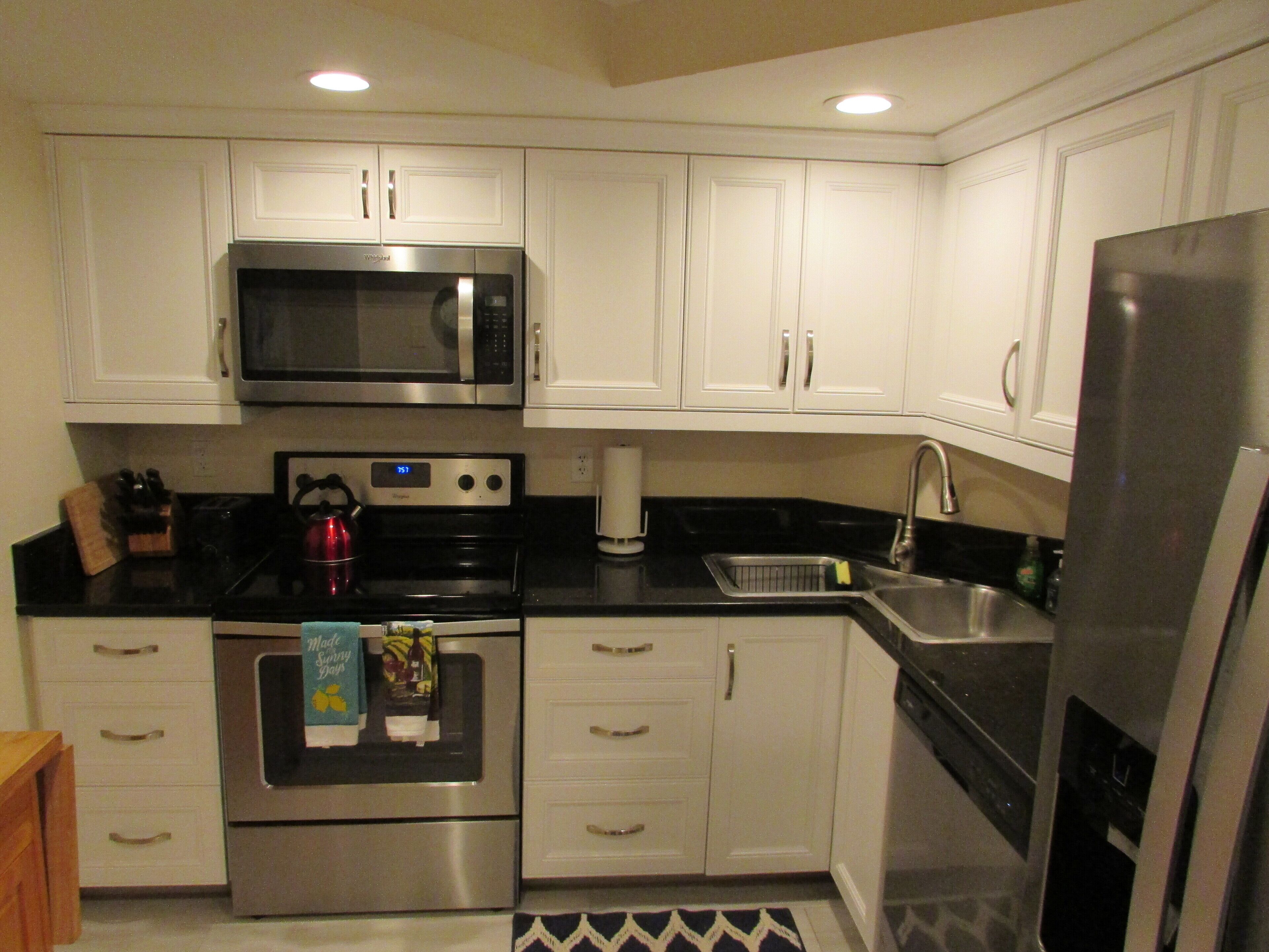 A kitchen with white cabinets, a stainless steel microwave, an oven, a sink, and a refrigerator.