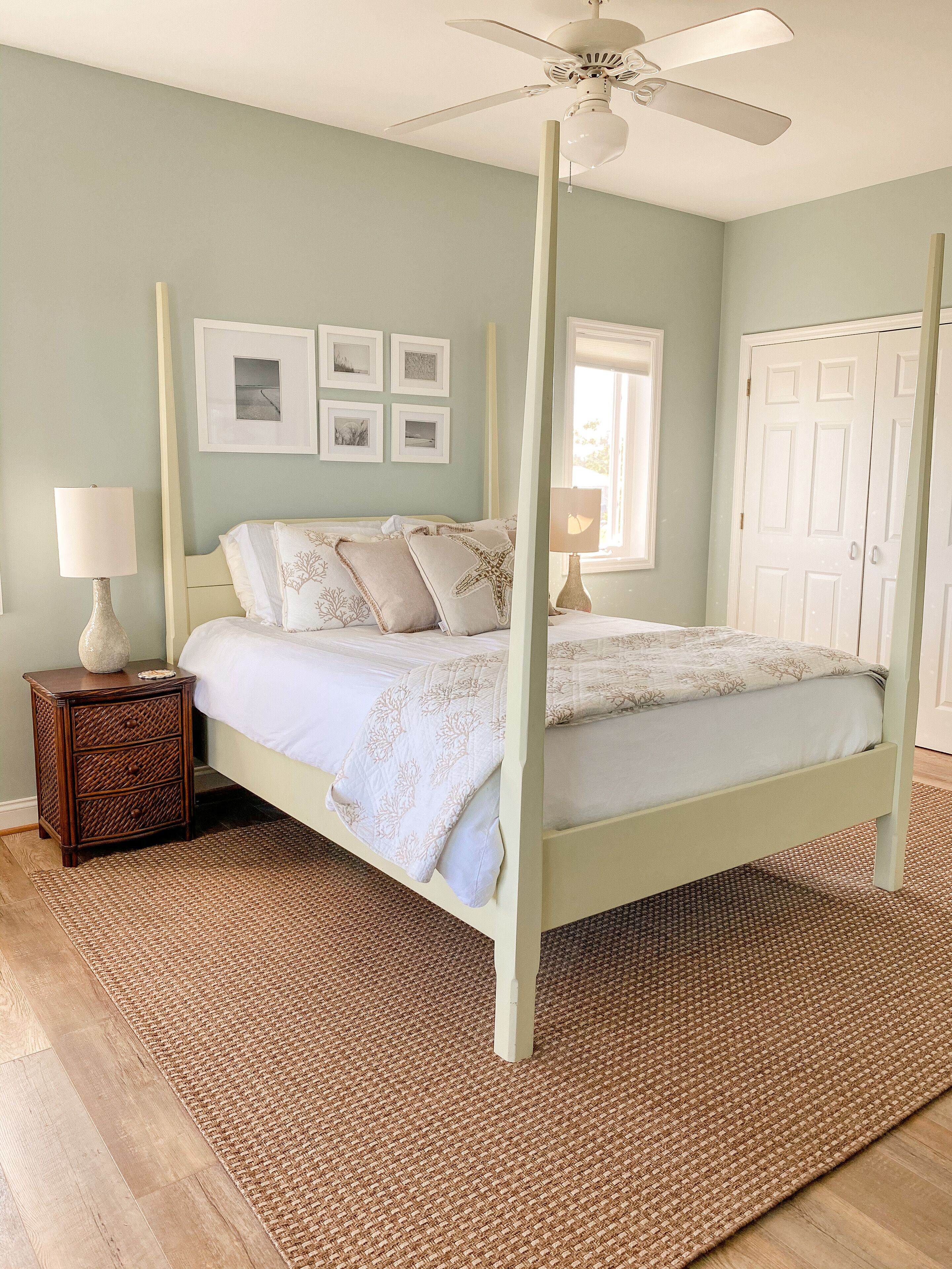 A bedroom with a four-poster bed, a ceiling fan, a nightstand with a lamp, and a woven rug.