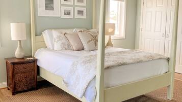 A bedroom with a four-poster bed, a ceiling fan, a nightstand with a lamp, and a woven rug.