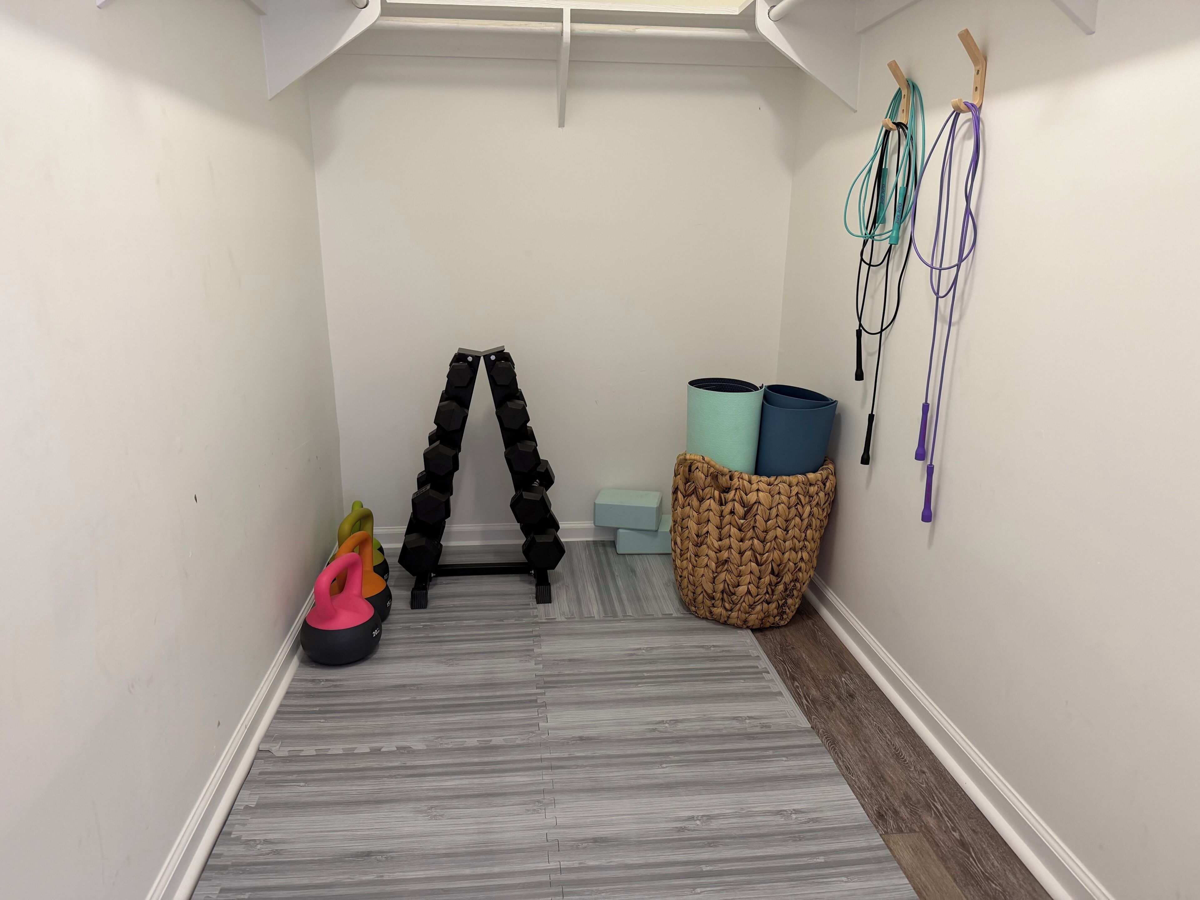 Un couloir doté d’un plancher en bois, d’un porte-haltères noir, d’un panier contenant des tapis de yoga et d’une corde à sauter fixée au mur.