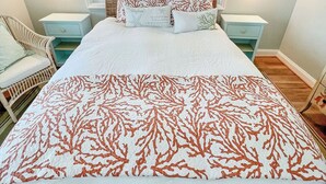 A bedroom with a large bed, two nightstands, a wicker chair, and a view of the ocean through three windows. - Peaceful Getaway with Amazing Views - Cape Lookout & Beaufort nearby - SLEEPS 8 (Davis)