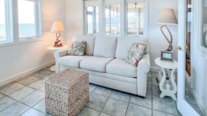 A spacious living room with a white sofa, a woven ottoman, and a ceiling fan. - Peaceful Getaway with Amazing Views - Cape Lookout & Beaufort nearby - SLEEPS 8 (Davis)
