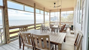 A covered outdoor deck with wooden furniture, a ceiling fan, and large windows offering a view of the sea. - Peaceful Getaway with Amazing Views - Cape Lookout & Beaufort nearby - SLEEPS 8 (Davis)