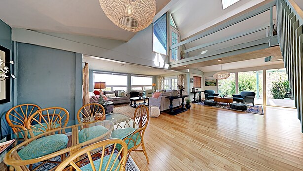 A spacious living area with a dining table, chairs, sofas, and a large window providing natural light. - Haleakala Sunrise Home, Kula, Maui, Hawaii (Kula)