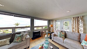 A spacious living room with two sofas, a coffee table, and a fireplace. Large windows offer a view of the outdoors. - Haleakala Sunrise Home, Kula, Maui, Hawaii (Kula)