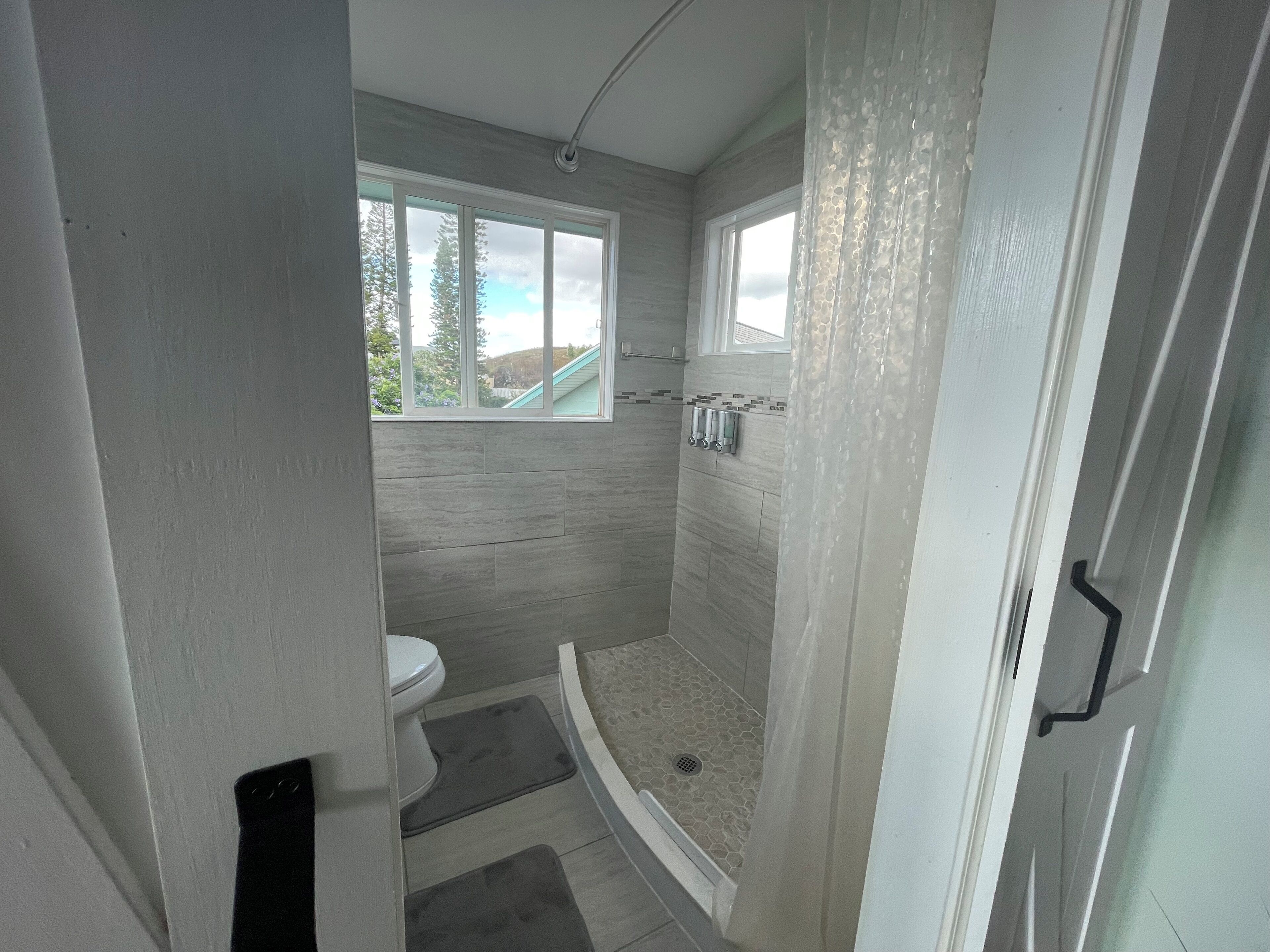 A modern bathroom with a shower, toilet, and a window.