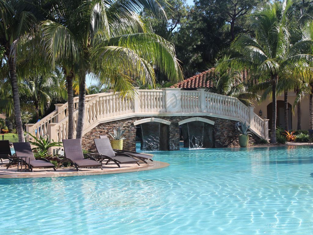 Ein Pool mit einer Steinbrücke, Palmen und Liegestühlen.