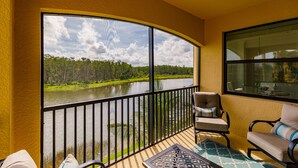 A balcony with a view of a lake and forest, furnished with two chairs and a table. - Escape the coldest and snowiest winter in years by "Springing" into Treviso Bay! (Naples)